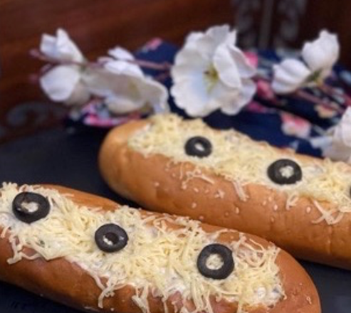 Two bread rolls with cheese and olives on a dark surface with flowers in the background.